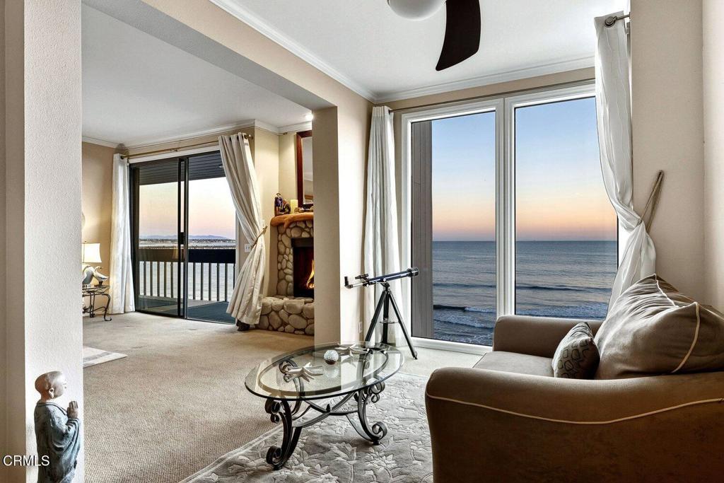Oceanfront living room with large windows, a stone fireplace, and a balcony.