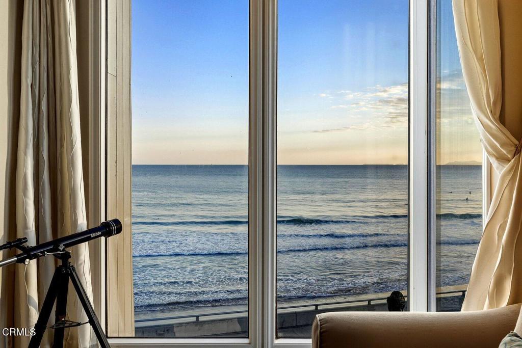 Living room with a telescope beside tall windows overlooking the ocean at golden hour.