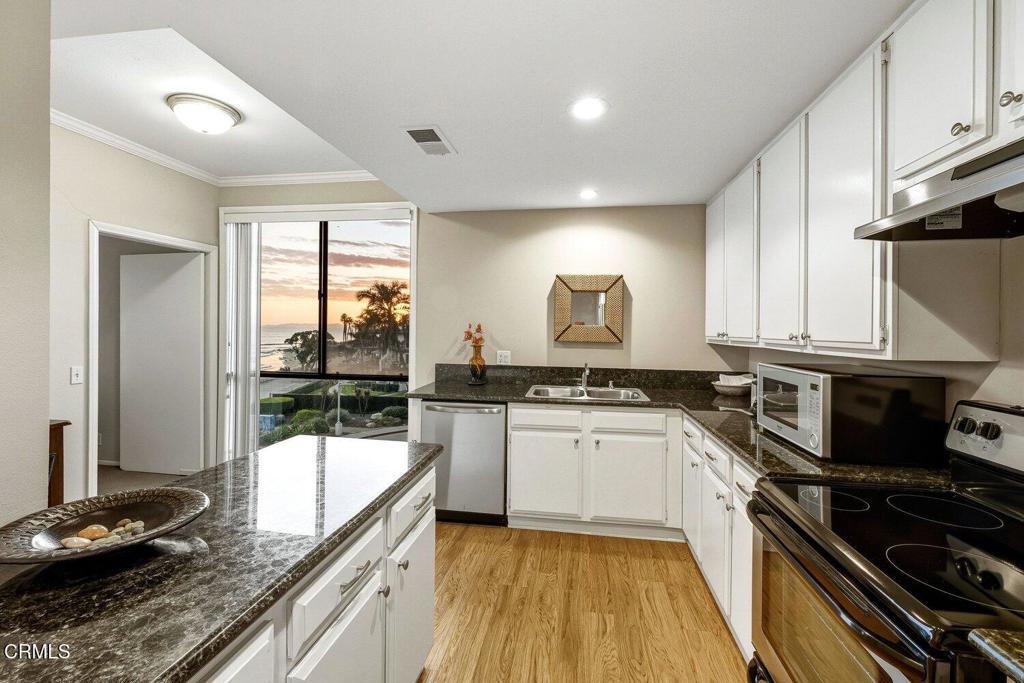 Kitchen with white cabinets and granite counters, opening to an ocean and palm-tree view at sunset.