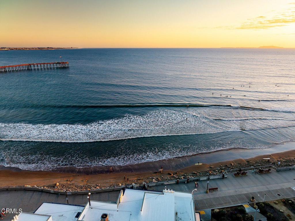 Ocean and beach at golden hour, with a pier extending into the water.