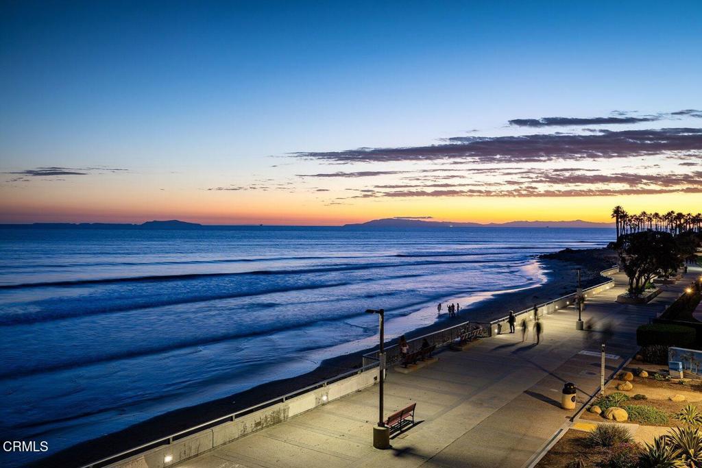 Ocean waves and beachfront promenade at sunset, viewed from above.