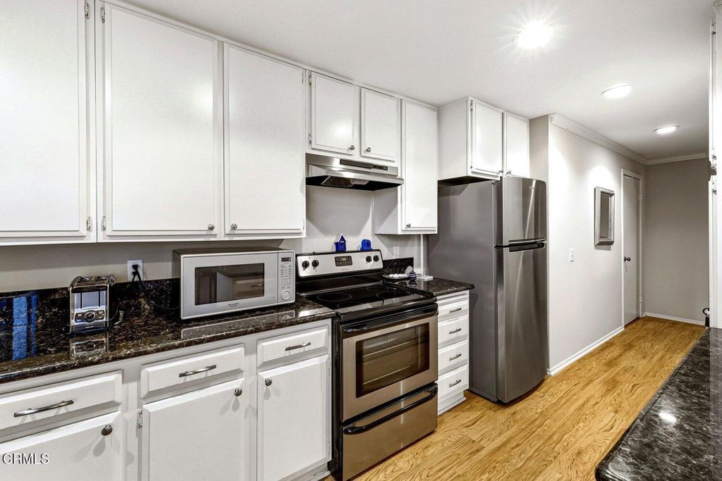 Kitchen with white cabinets, dark stone counters, stainless steel appliances, and hardwood floors.