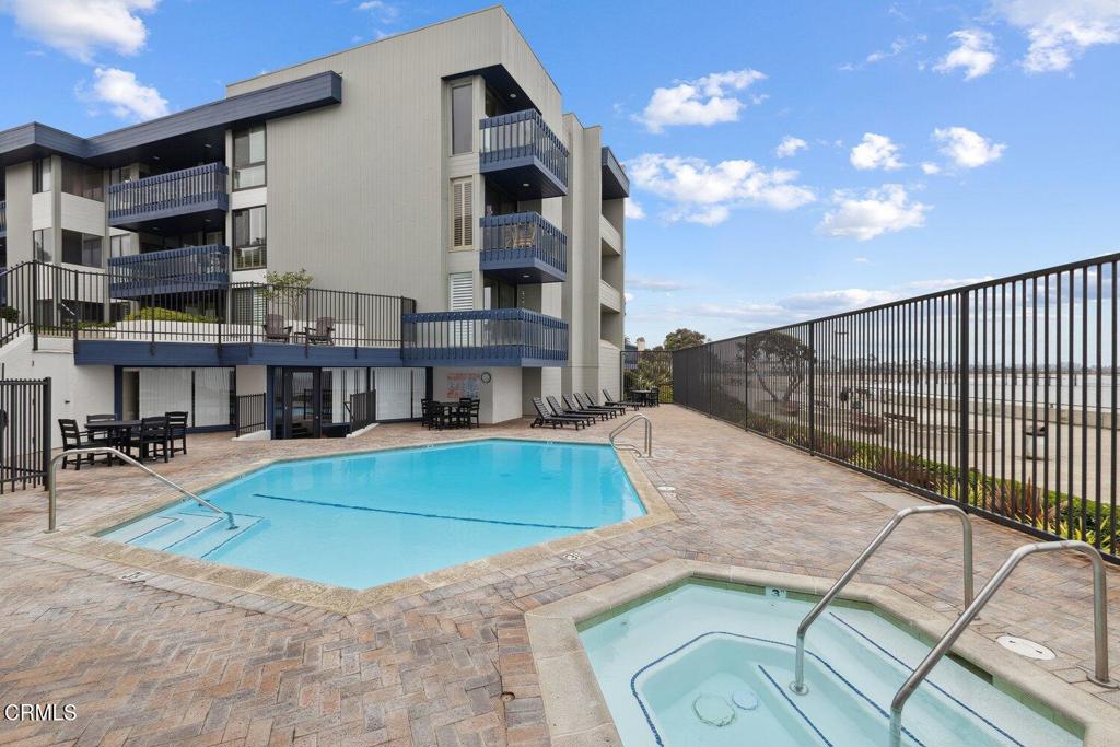 Condominium pool and spa beside a modern building, with brick paving and lounge chairs.