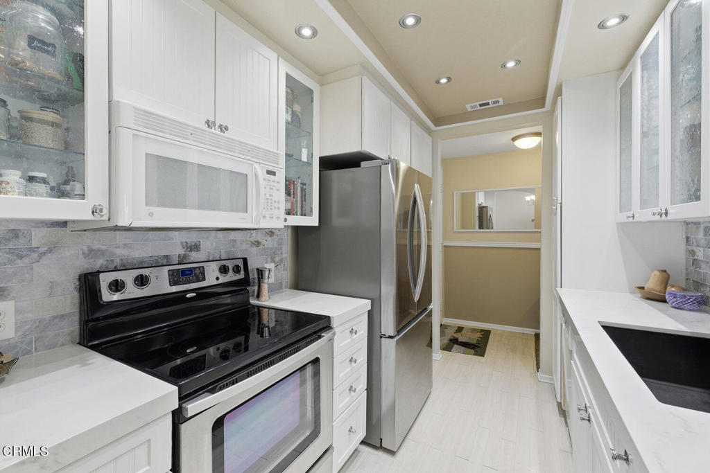 Bright galley kitchen with white cabinetry, gray tile backsplash, and stainless steel appliances.