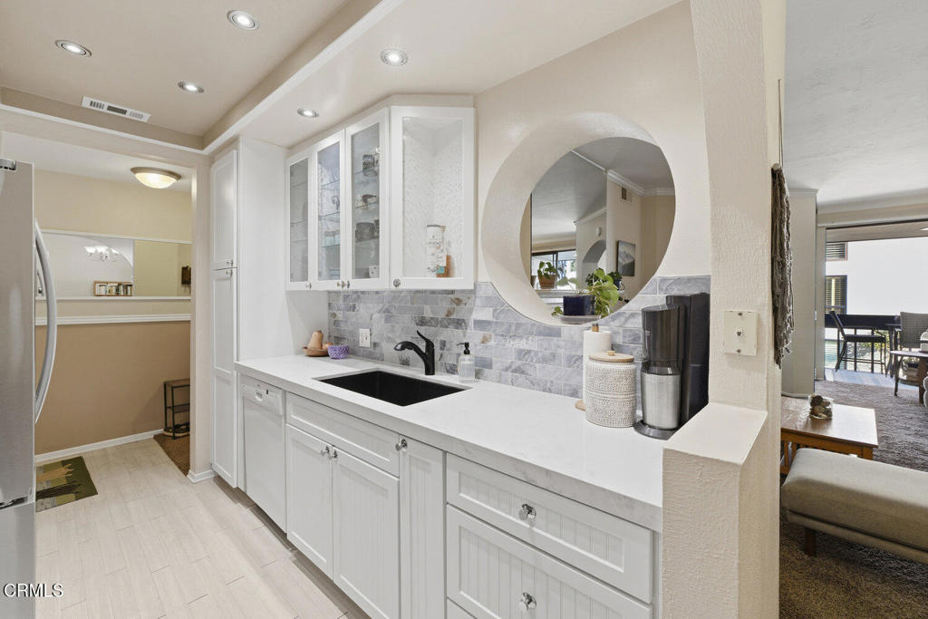 Kitchen with white cabinetry, gray marble backsplash, long sink counter, and round mirror.