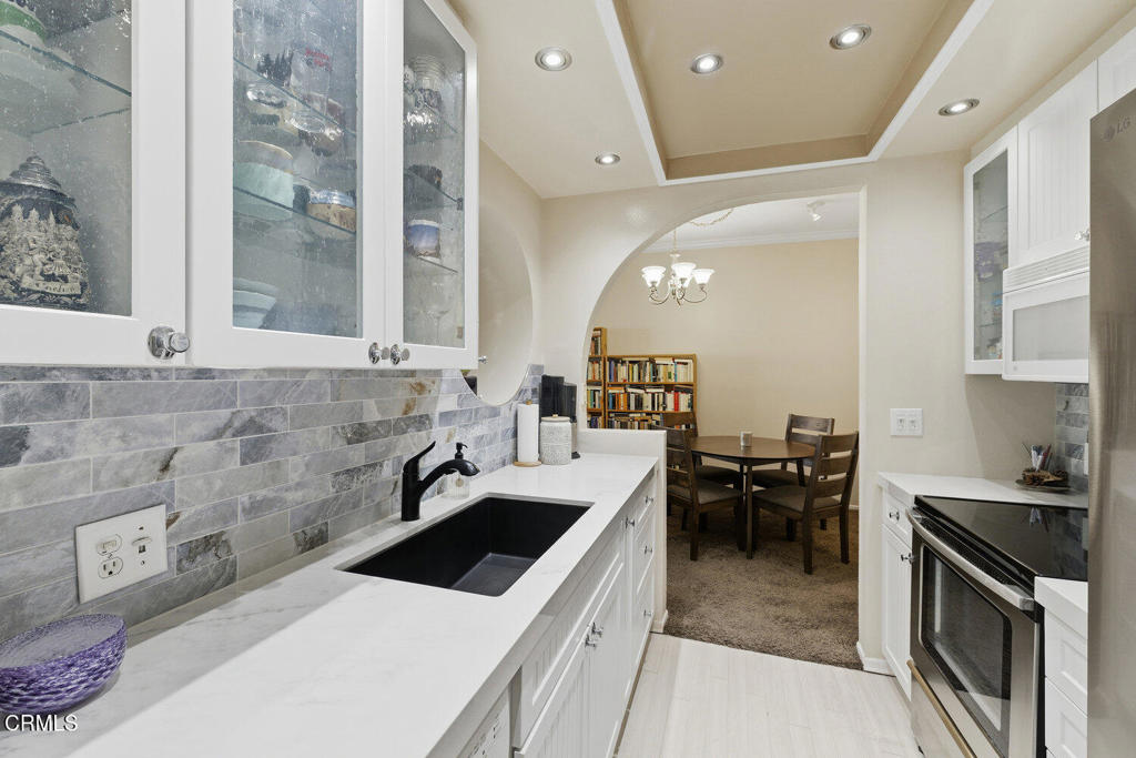 Kitchen with gray tile backsplash, marble-look counters, black sink, and arched opening to a dining nook.