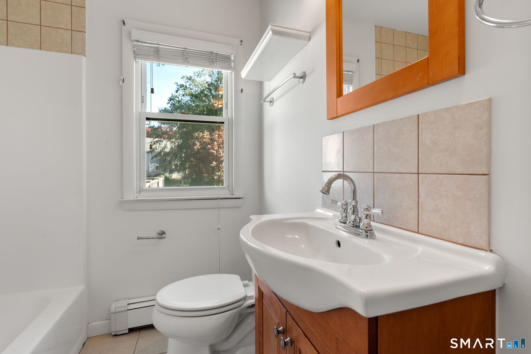 Bathroom with a wood vanity, beige tile accents, and a window above the toilet.