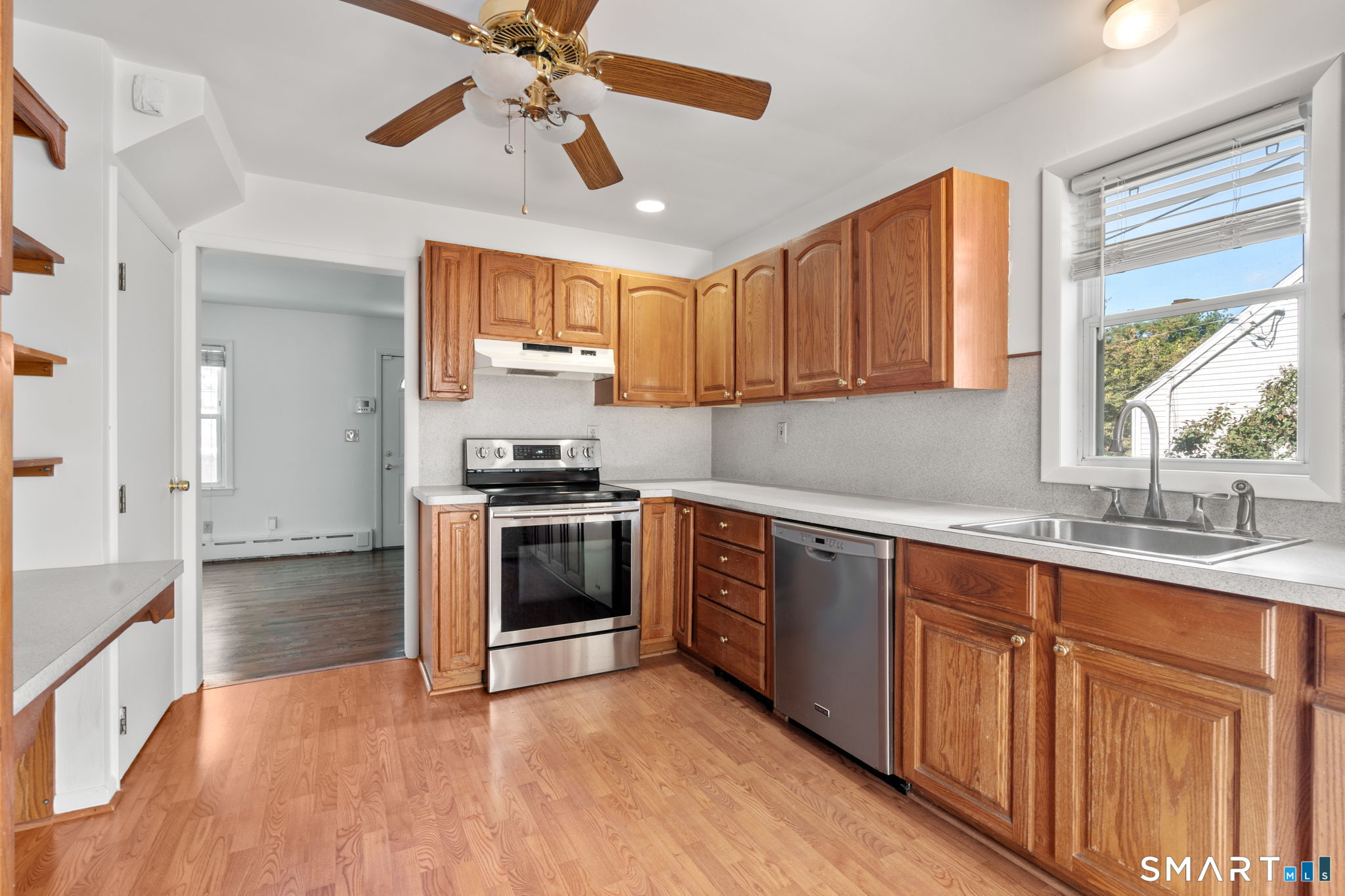 Kitchen with honey-toned wood cabinets, stainless steel appliances, and a sink beneath a bright window.
