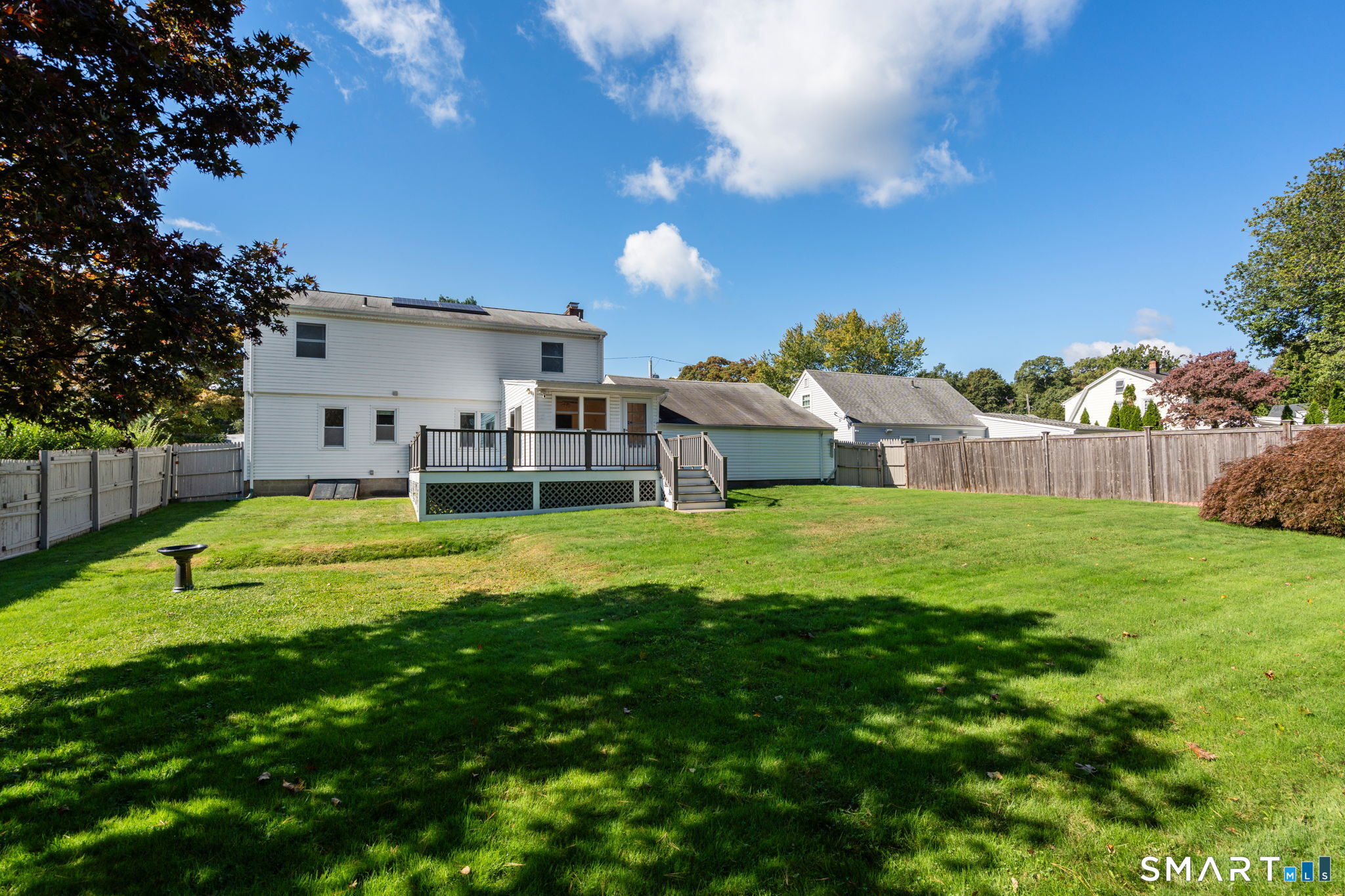 Rear of a white two-story house with a raised deck, fenced lawn, and rooftop solar panels.