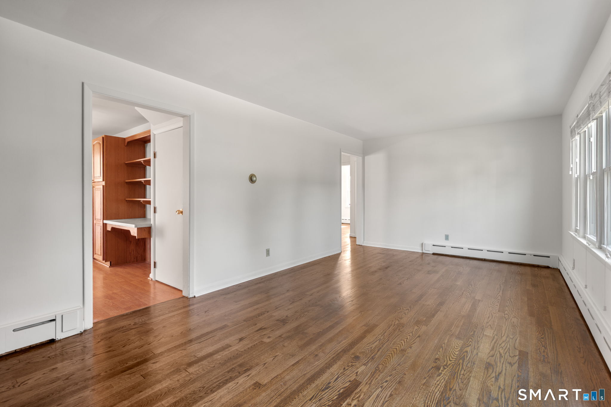 Unfurnished room with hardwood floors, tall windows, and a built-in wood desk and shelves.