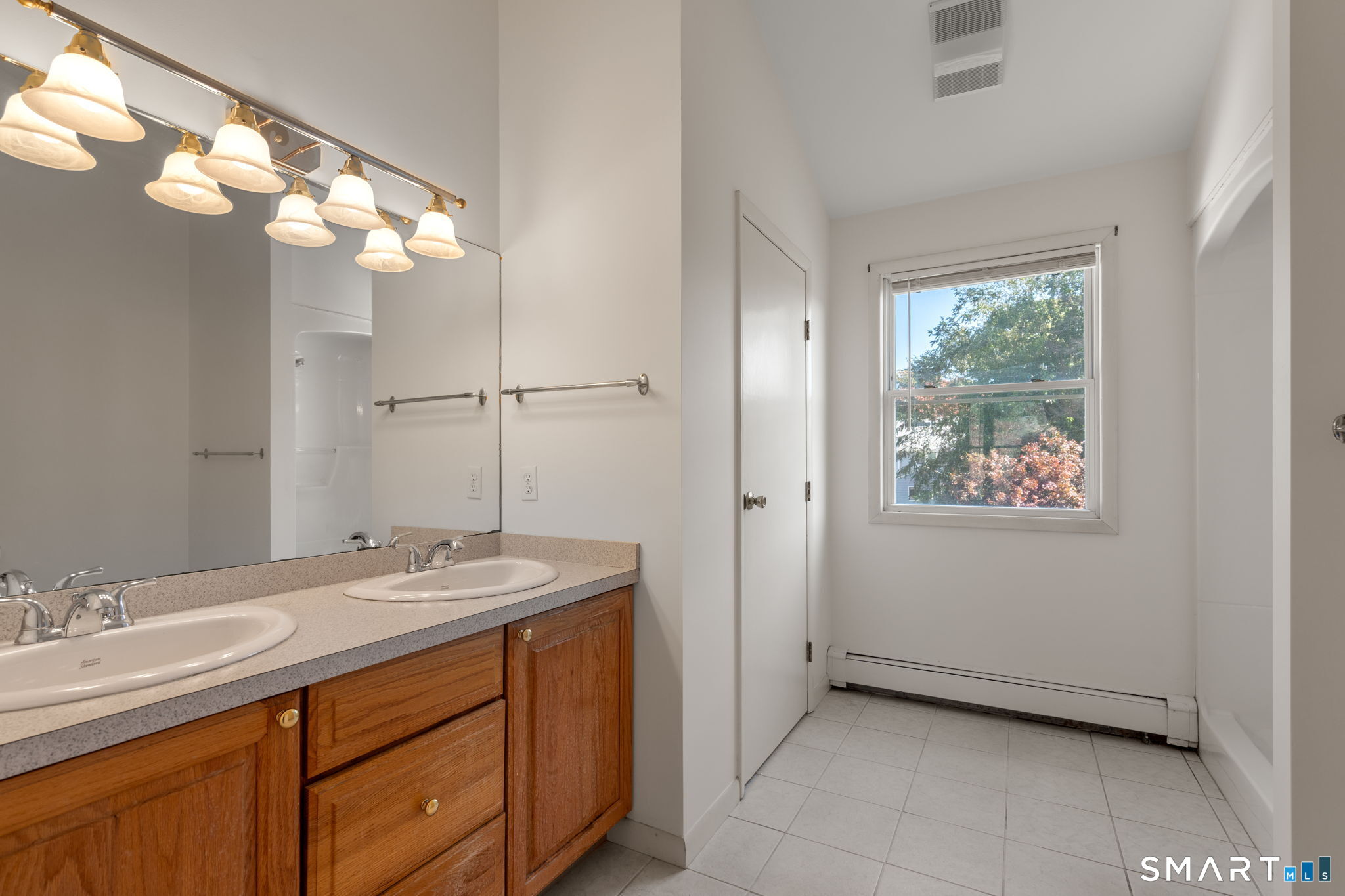 Bathroom with a double-sink wood vanity, large mirror, and window overlooking trees.