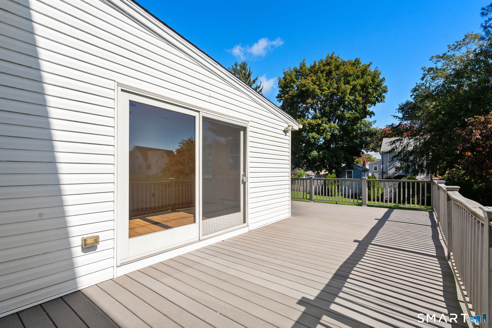 Raised deck beside a white-sided house, with a large sliding glass door and railings.