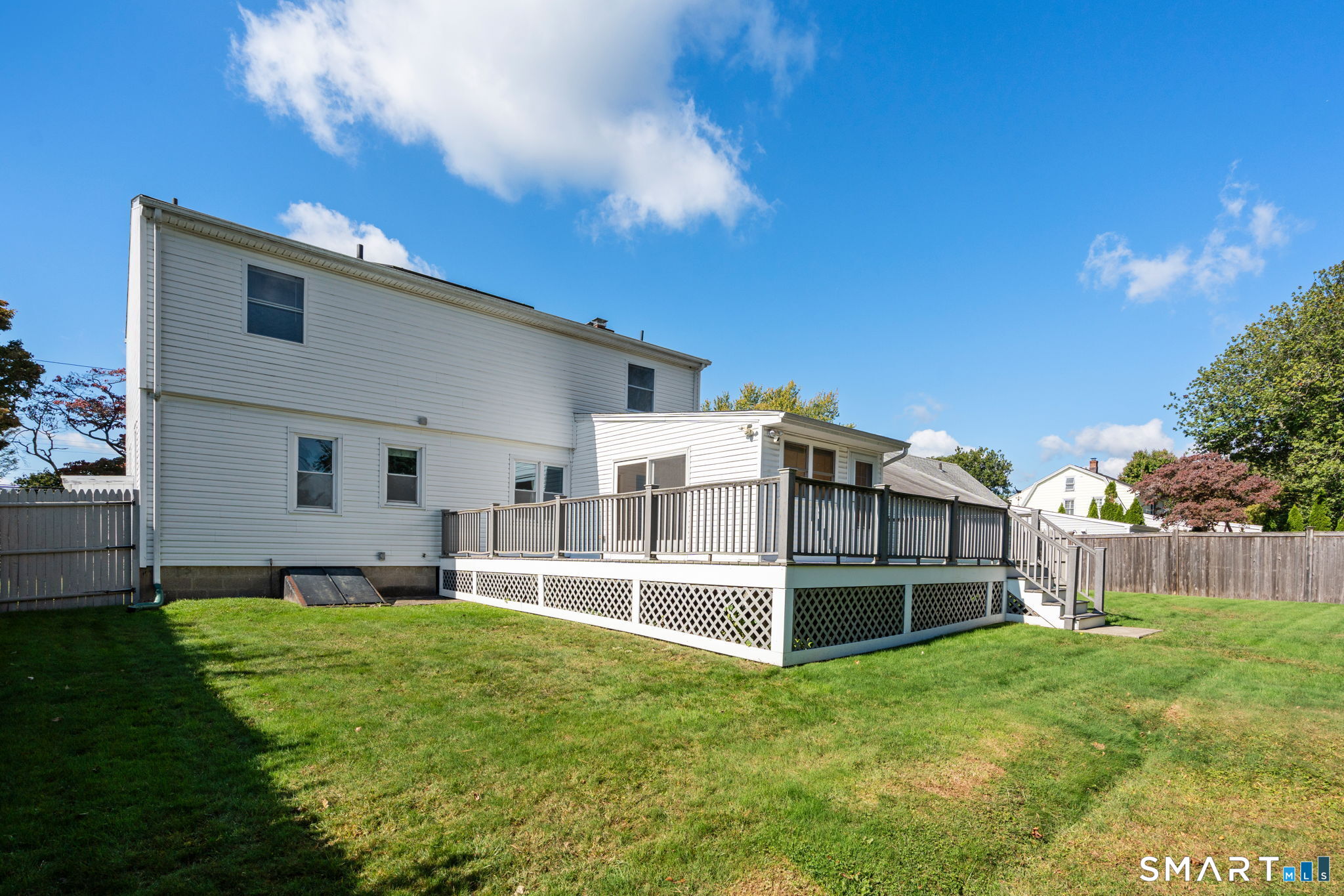Rear of a white two-story house with a raised deck overlooking a fenced lawn.