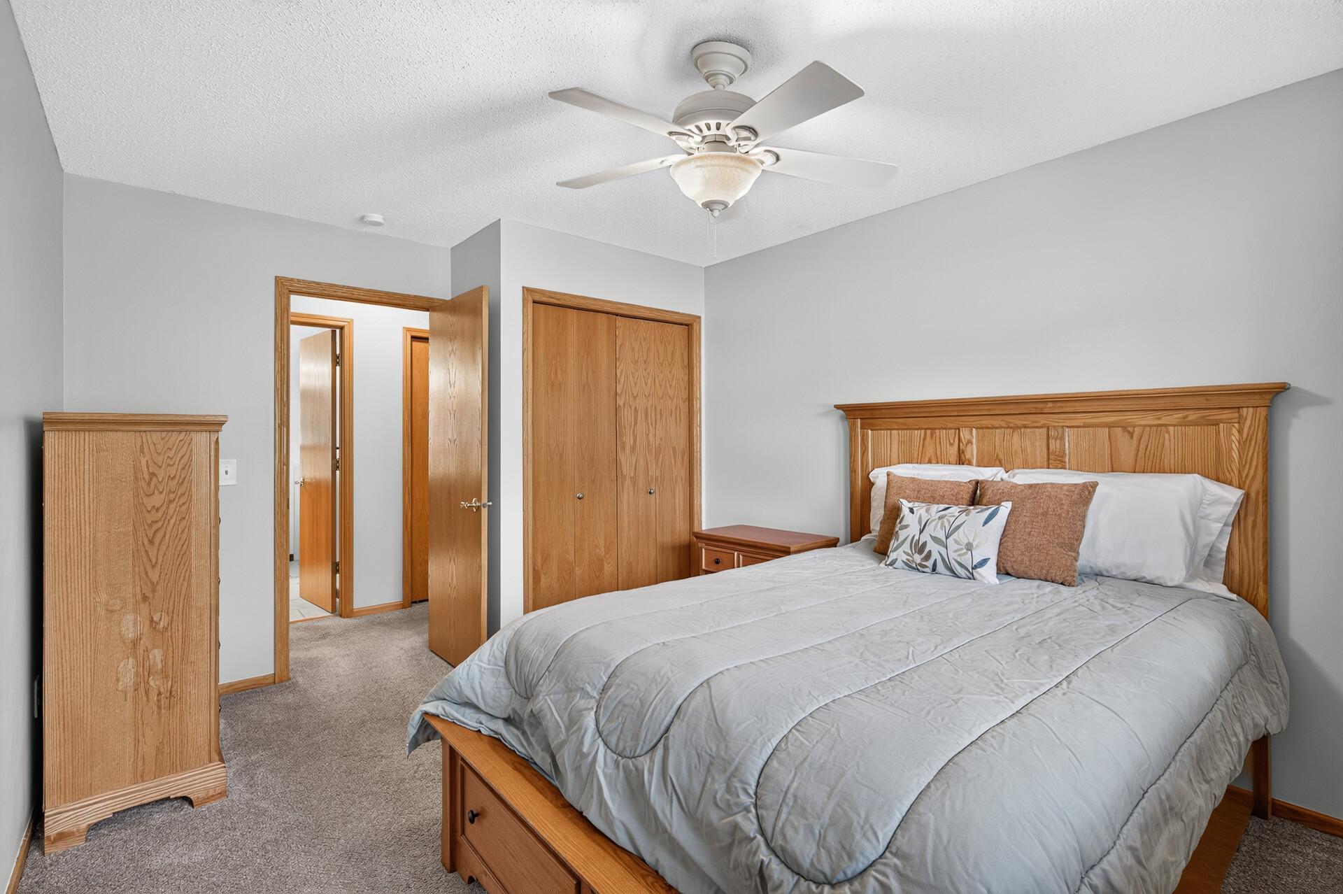 Bedroom with a gray-covered bed, wood furniture, and ceiling fan.