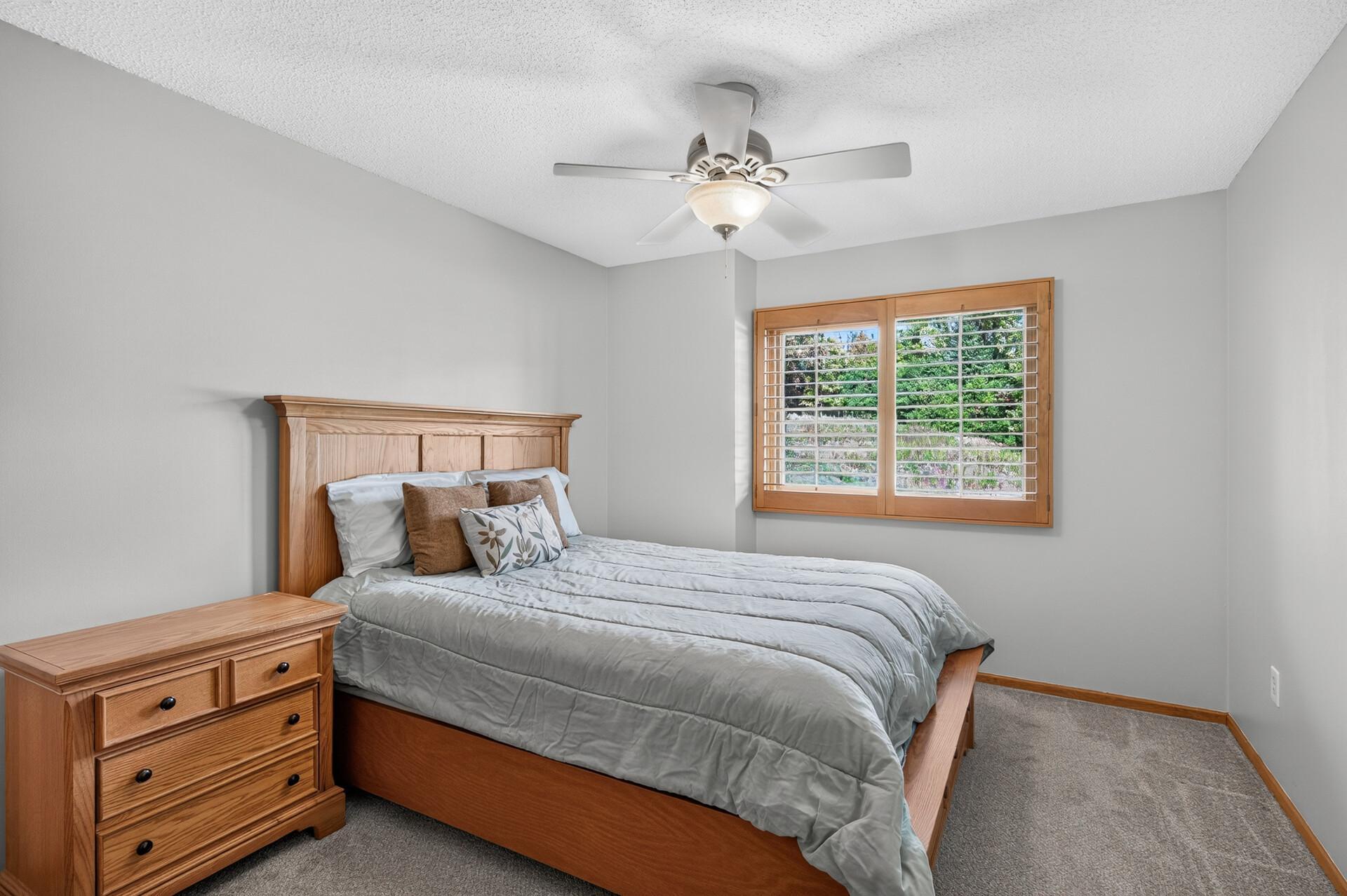 Bedroom with gray bedding, wooden furniture, and a window with plantation shutters.