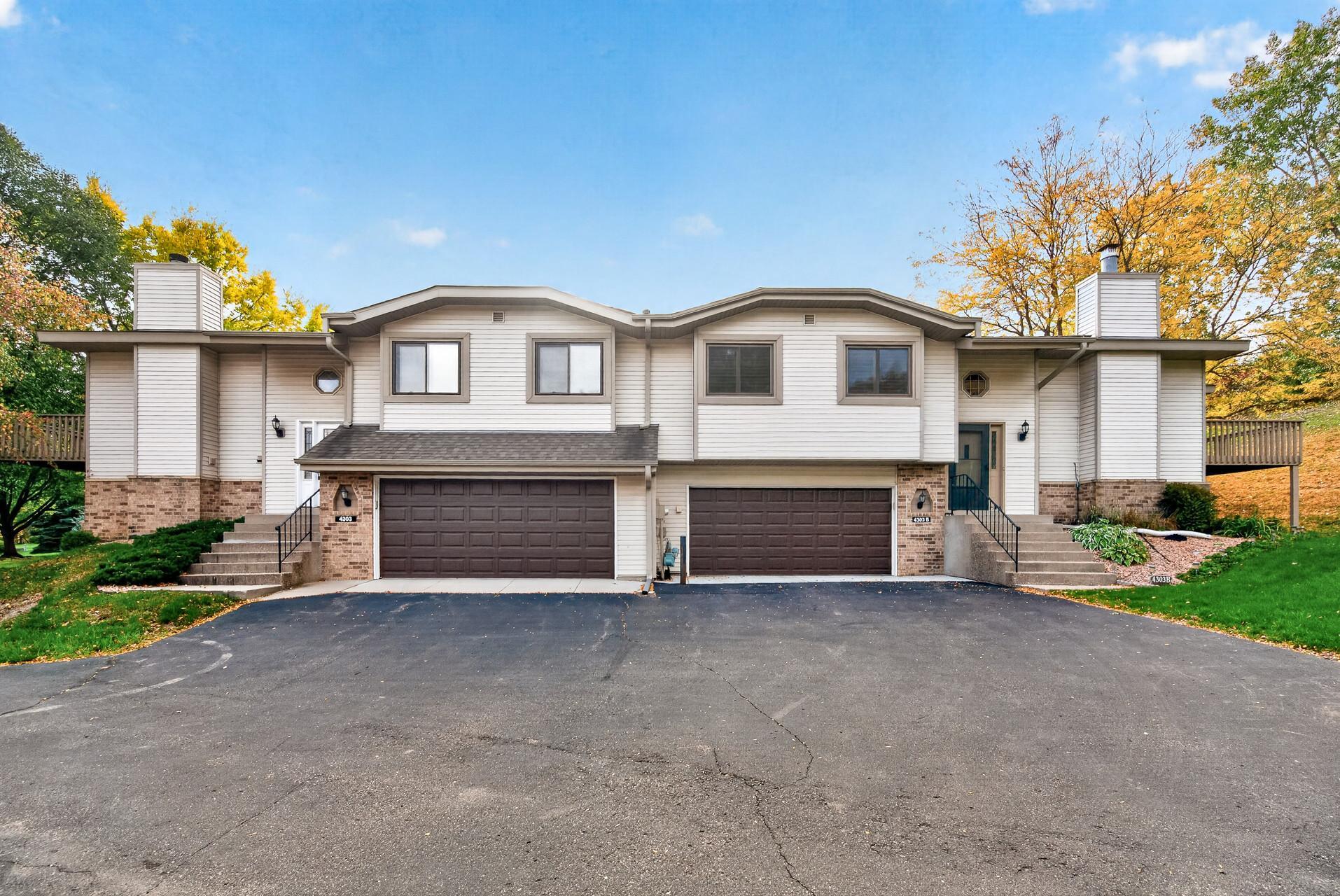 Two-unit townhouse exterior with twin garages, brick lower walls, and autumn trees.
