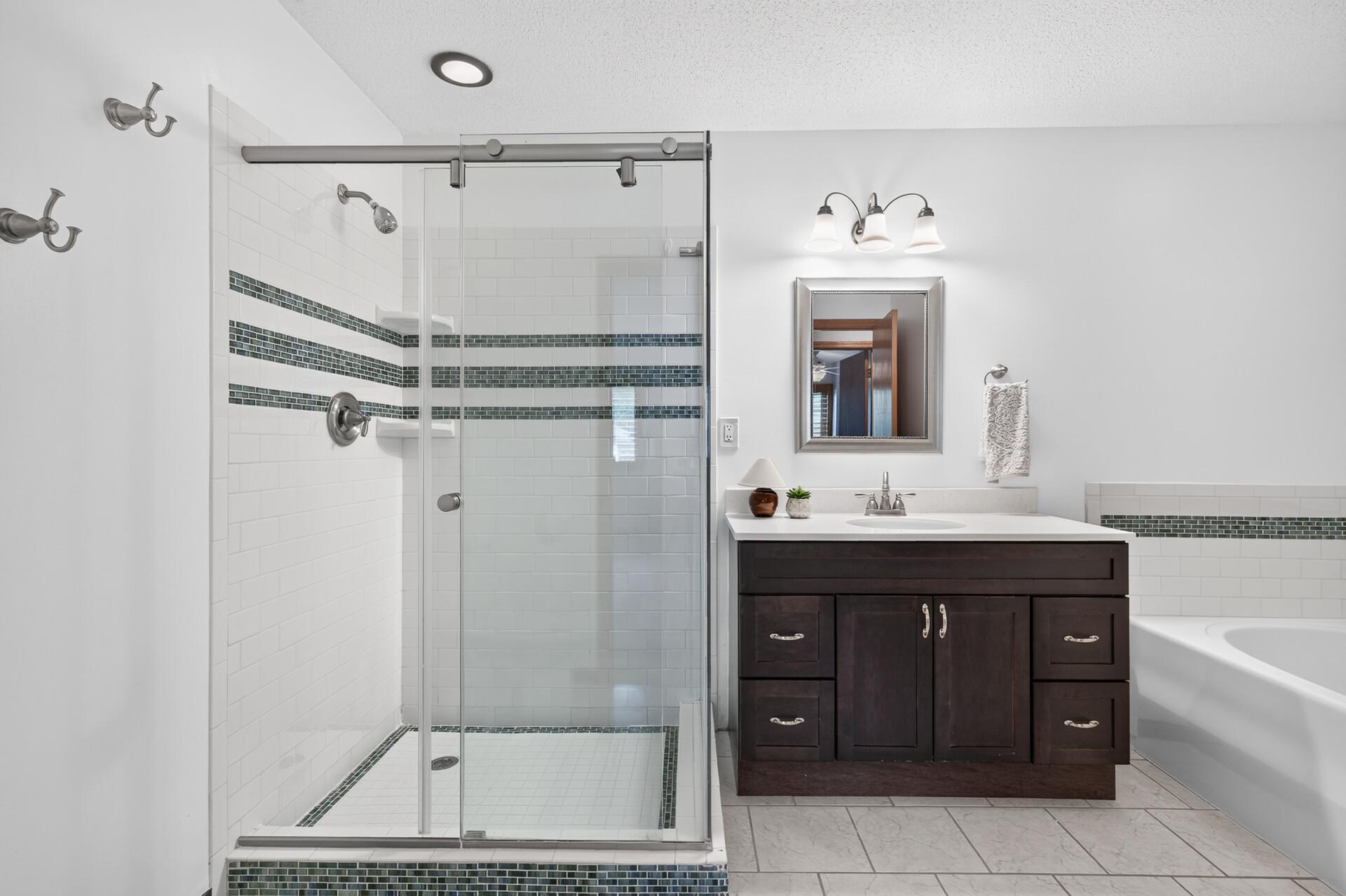 Bathroom with a glass walk-in shower, dark mosaic tile accents, and a dark wood vanity beside a bathtub.