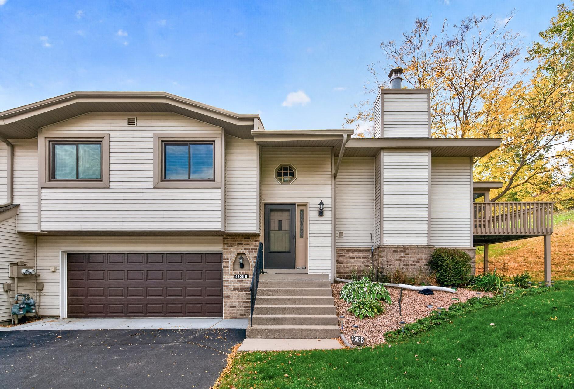 Split-level home with a double garage, raised front steps, and a covered deck amid autumn foliage.