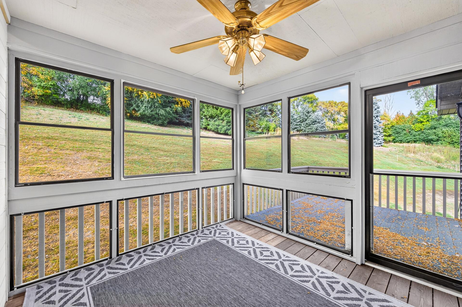 Enclosed sunroom with large windows, a ceiling fan, and a leafy autumn yard view.