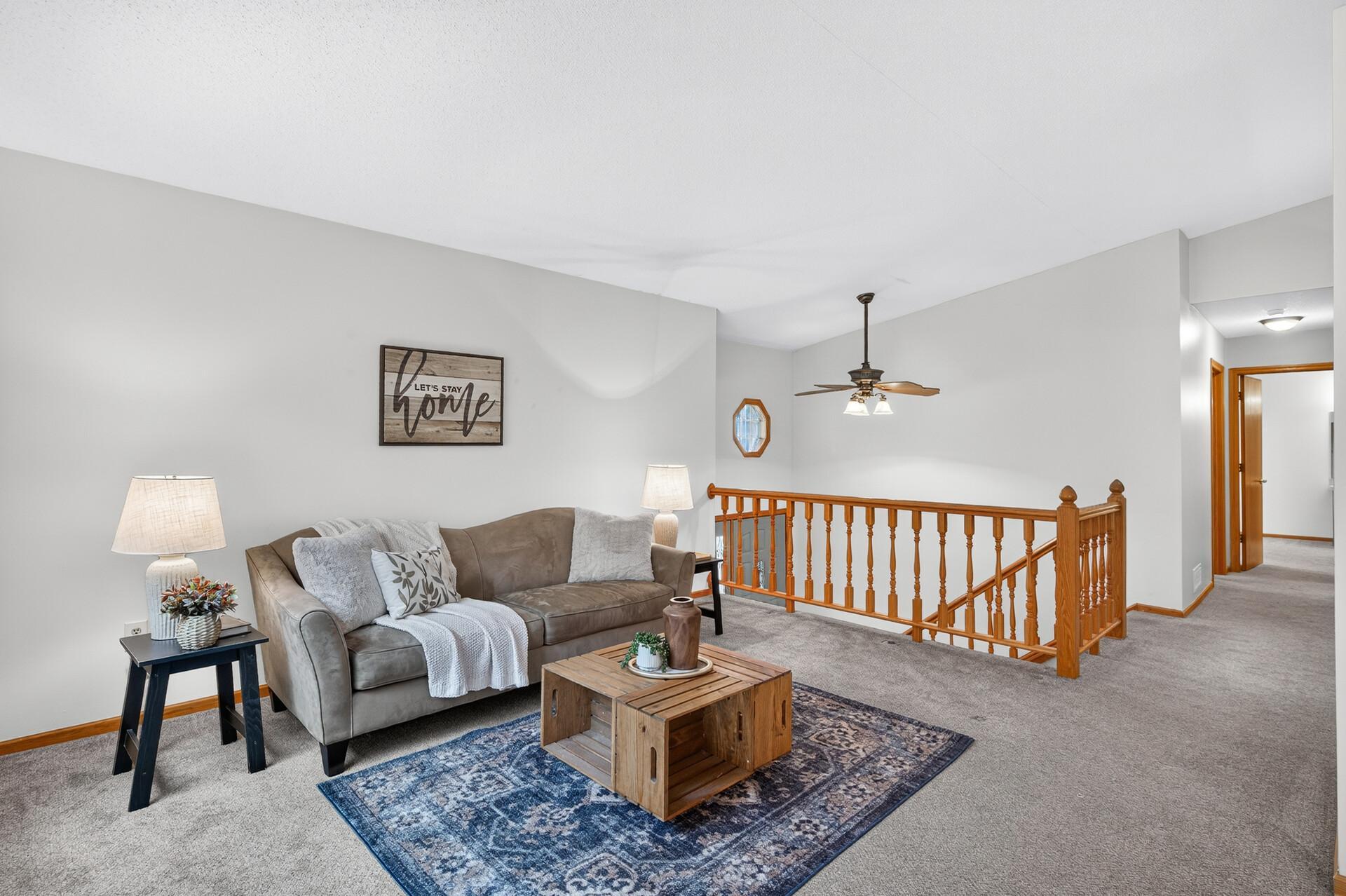 Living room with a gray sofa and blue rug beside a wooden-railed stair landing.