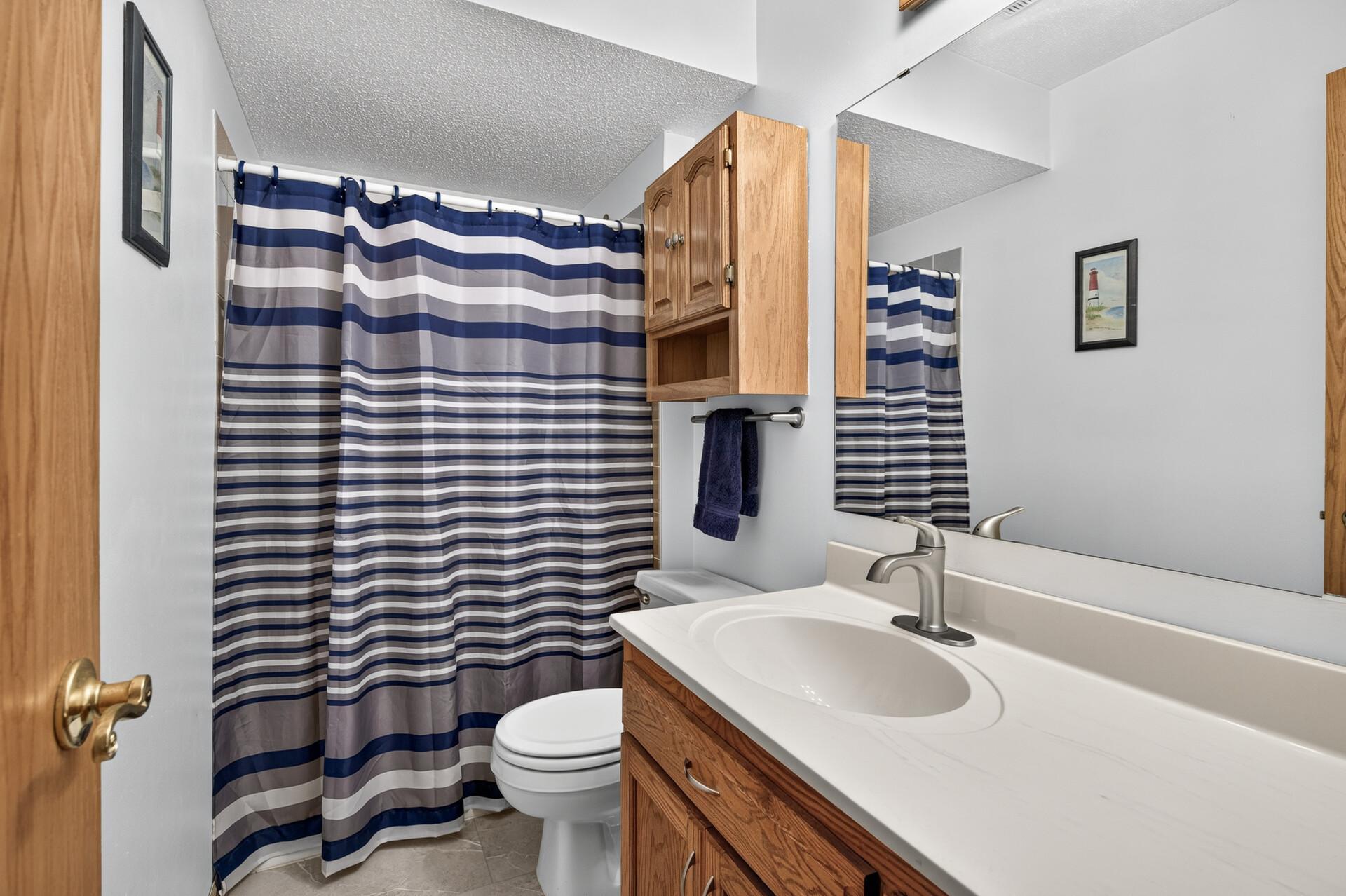 Bathroom with a wood vanity, white sink, toilet, and navy striped shower curtain.