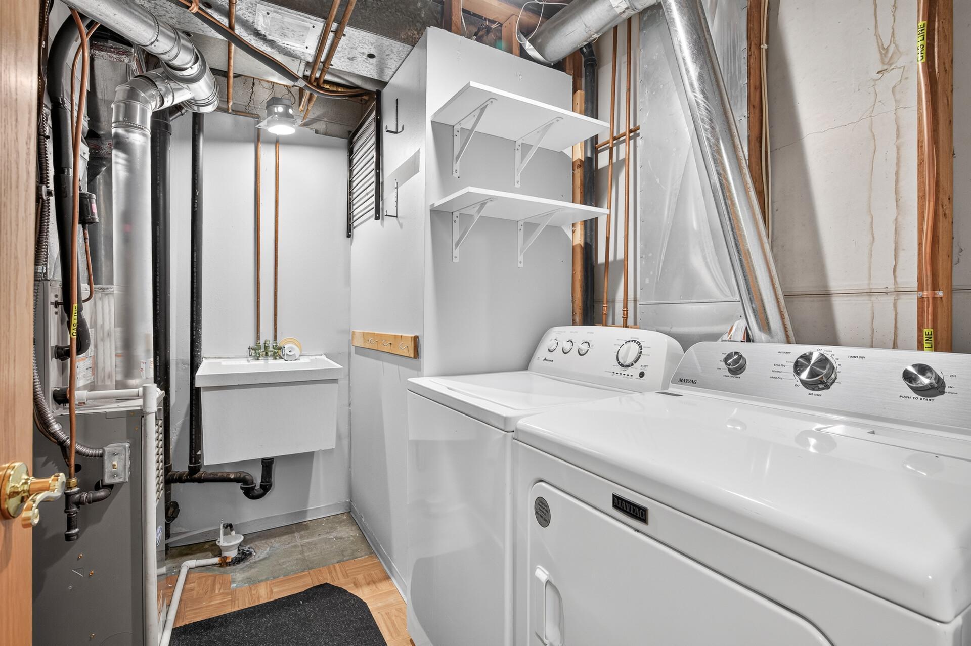 Laundry room with white washer and dryer, utility sink, and exposed pipes and ductwork.