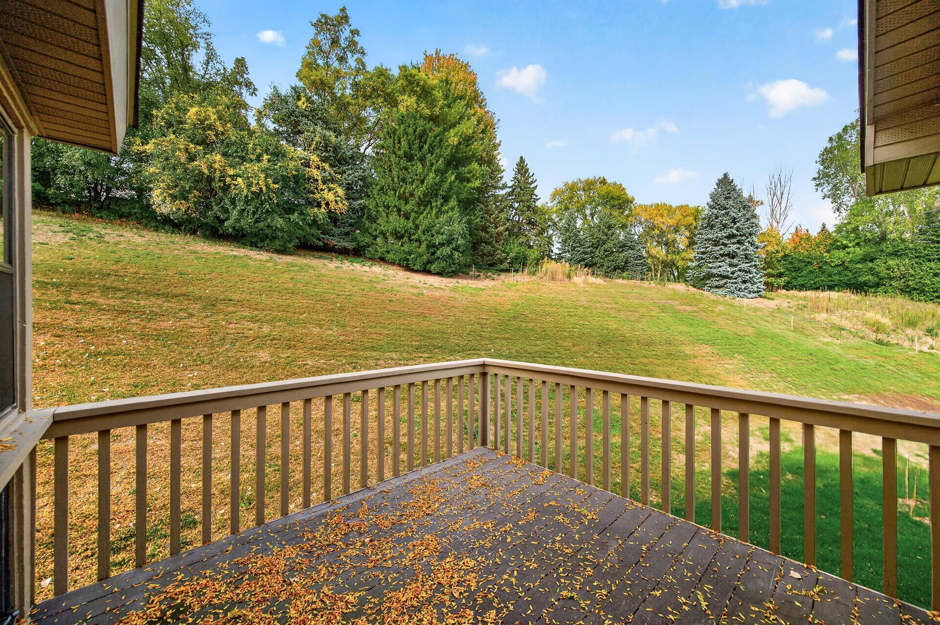 Raised wooden deck overlooking a sloping, tree-lined yard, with autumn leaves scattered across the deck.