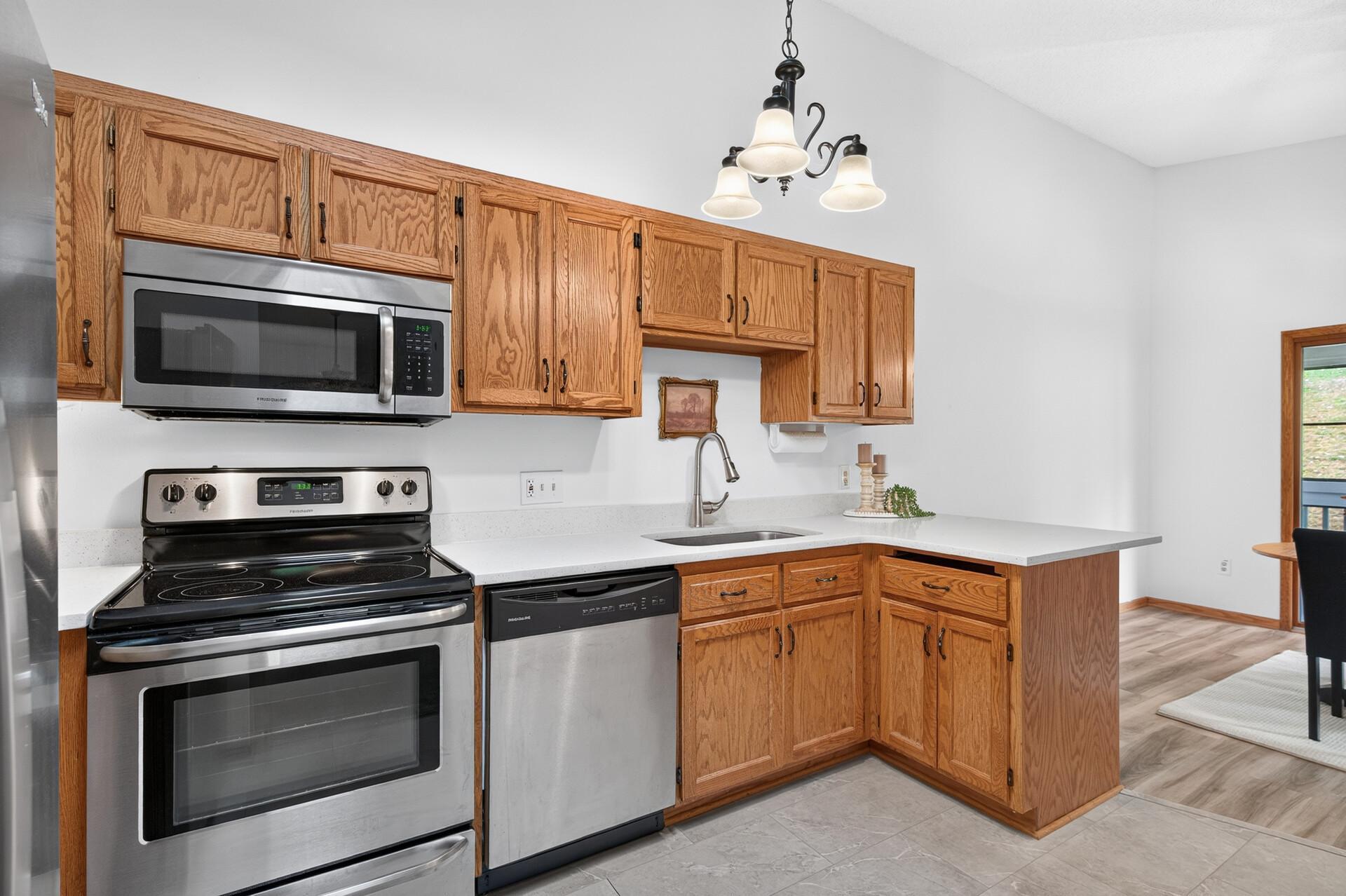Kitchen with oak cabinets, white counters, stainless appliances, and a sink beneath a three-light pendant.