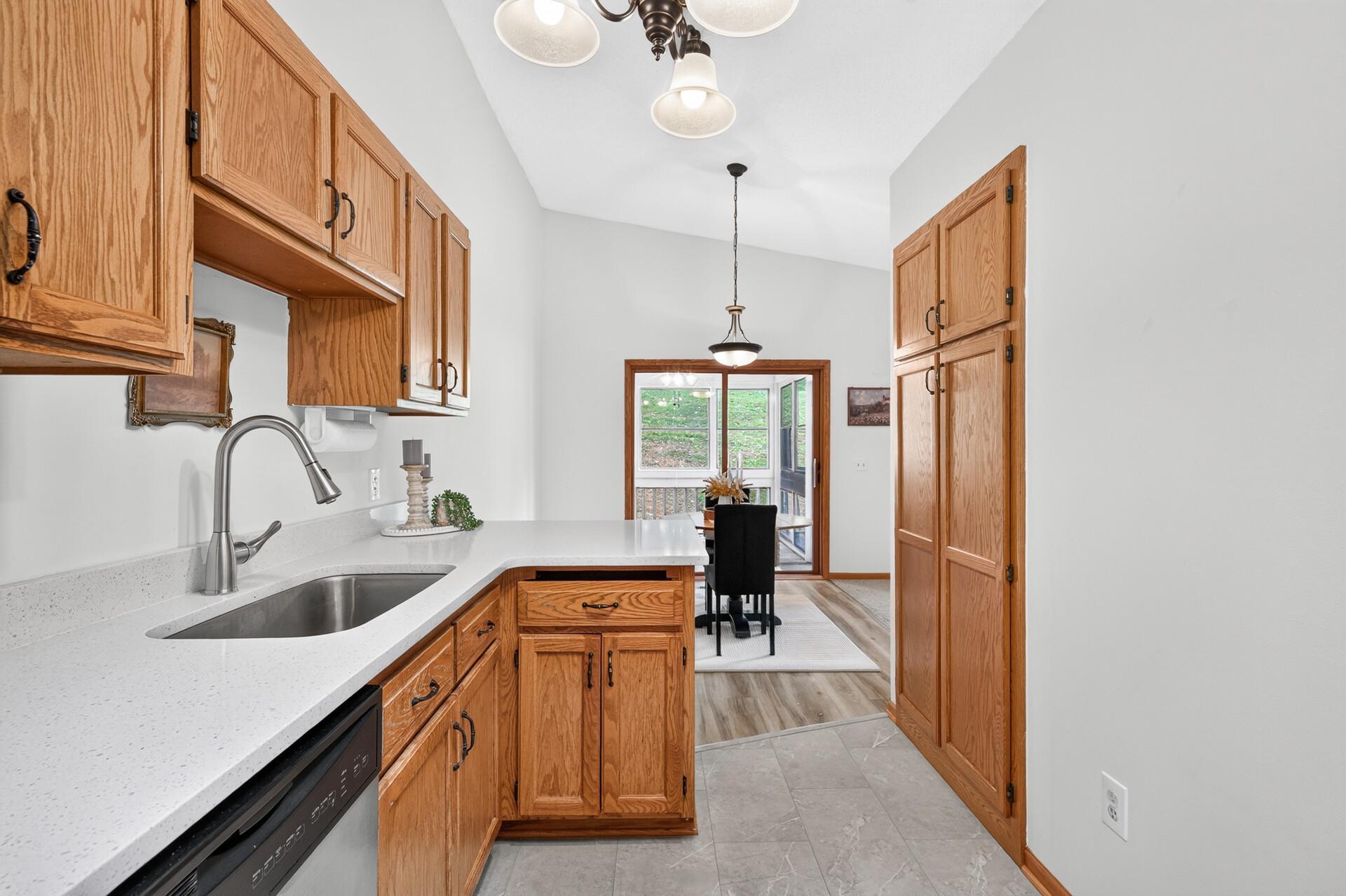 Kitchen with oak cabinets and white counters opening to a dining area and windowed porch.