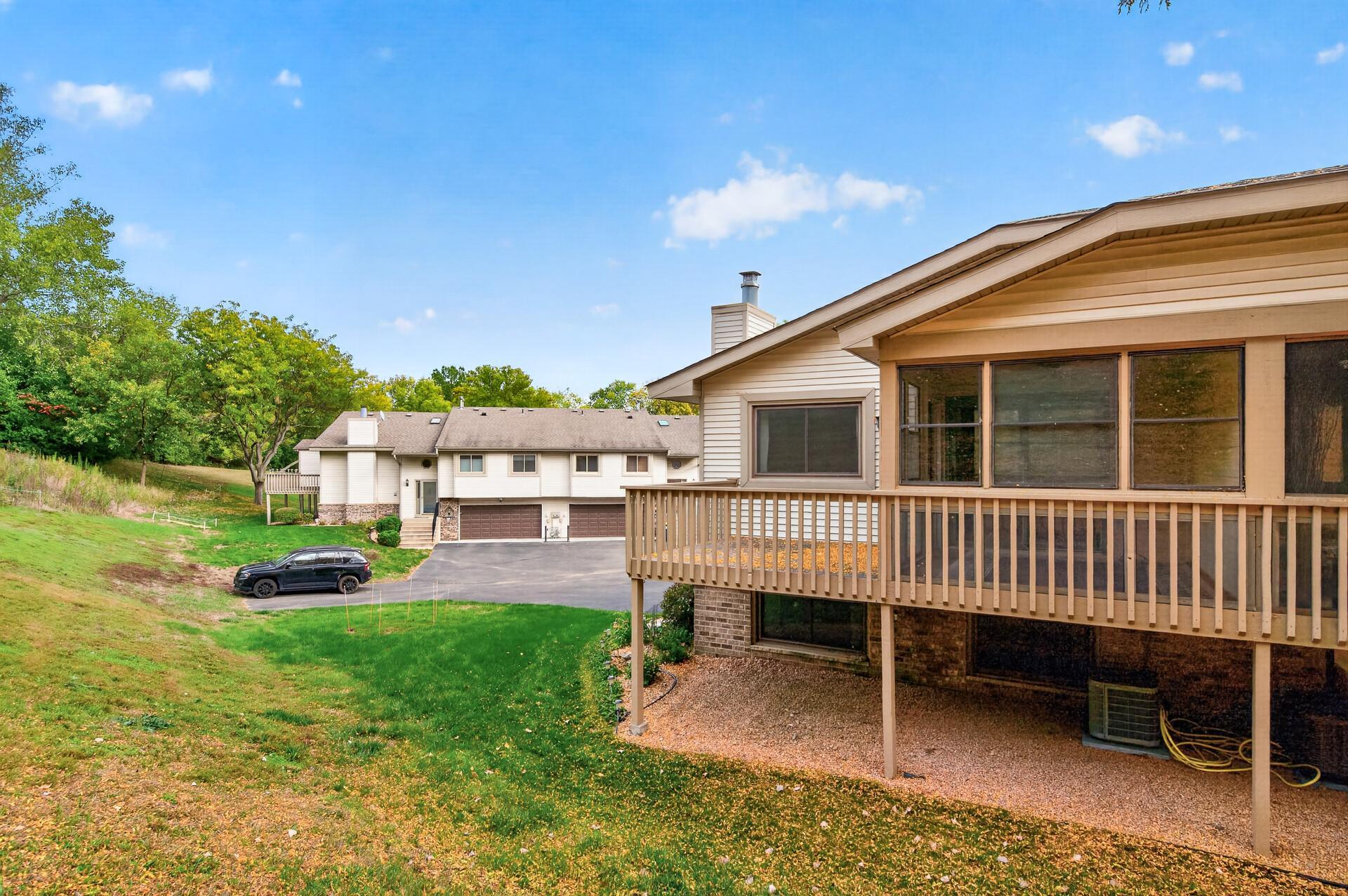 Multi-unit building with a raised wooden deck overlooking neighboring homes and a grassy slope.