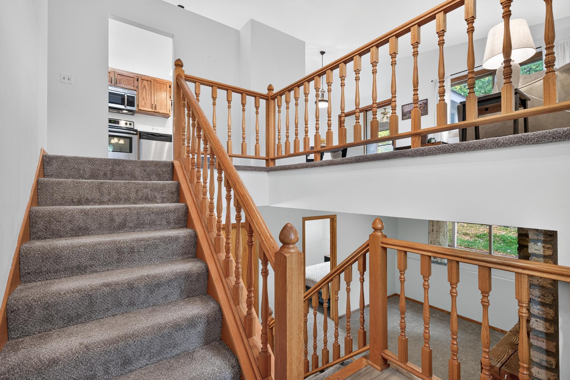 Carpeted staircase and landing with wooden railings, with the kitchen visible beyond.