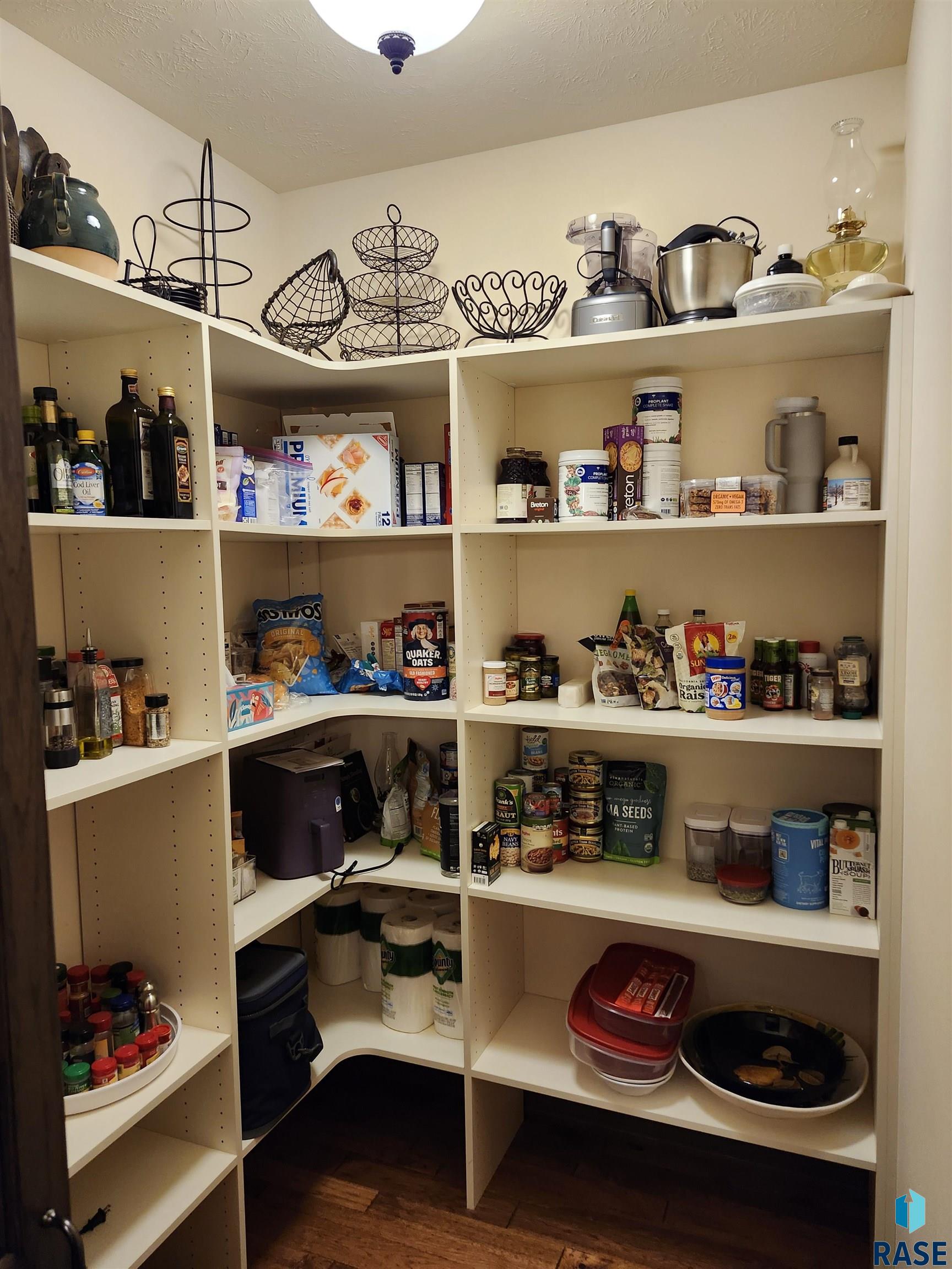 Walk-in pantry with stocked built-in shelves, wire baskets, cookware, and a dark wood floor.