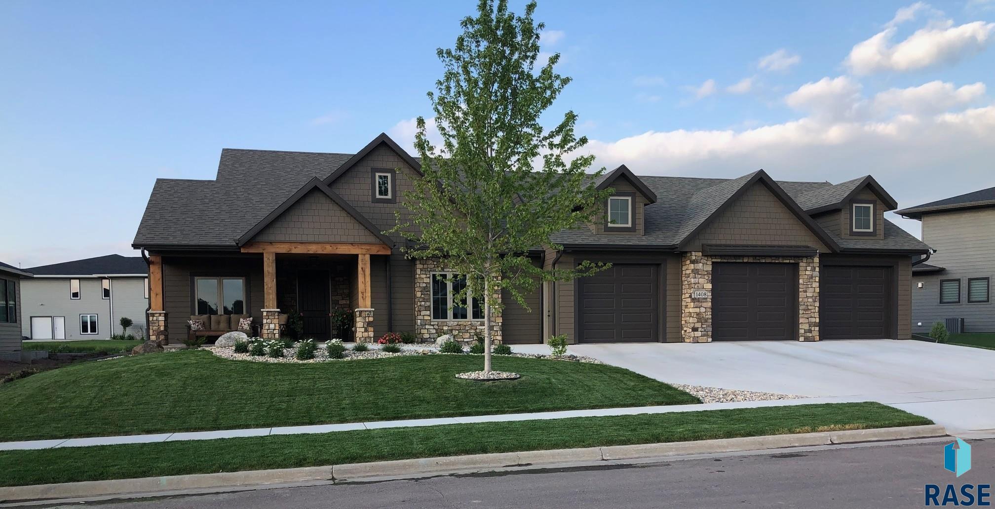 Brown stone-accented home with a covered porch, three-car garage, and landscaped front lawn.