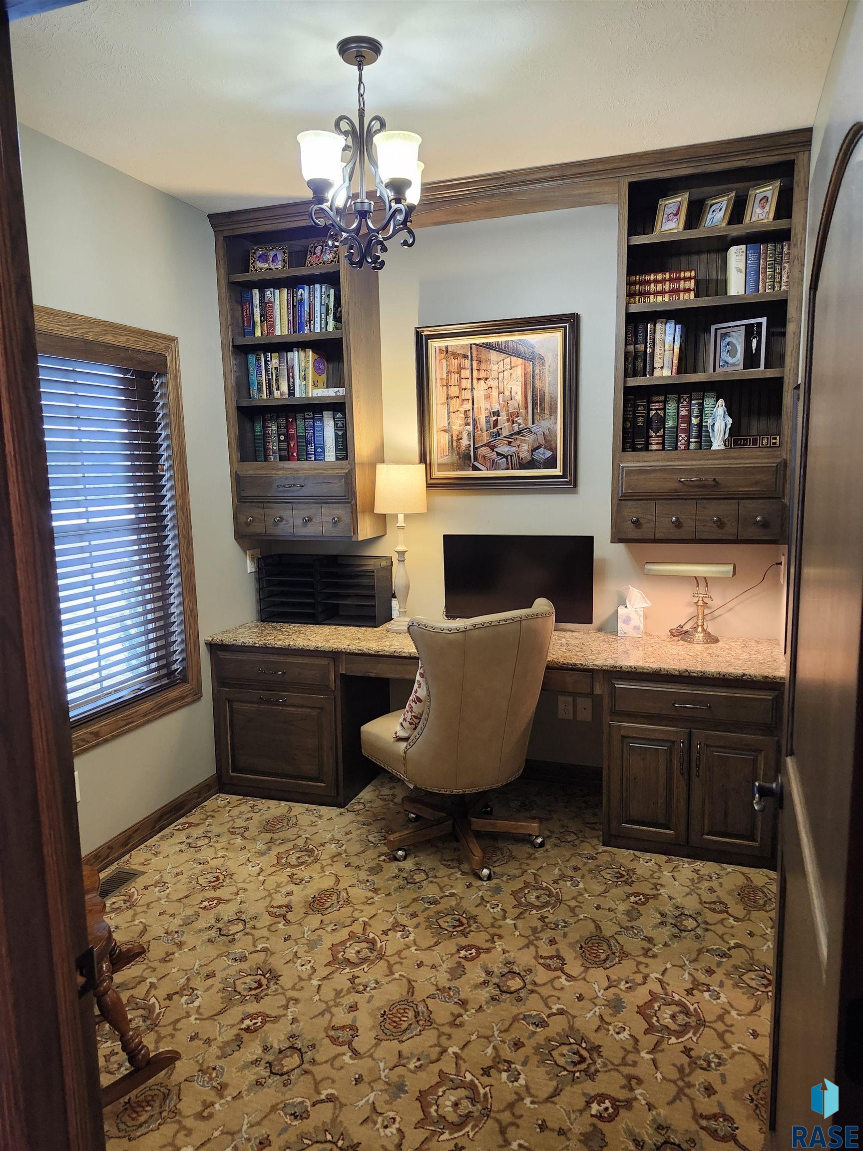 Home office with built-in bookcases and desk, granite countertop, and patterned carpet.