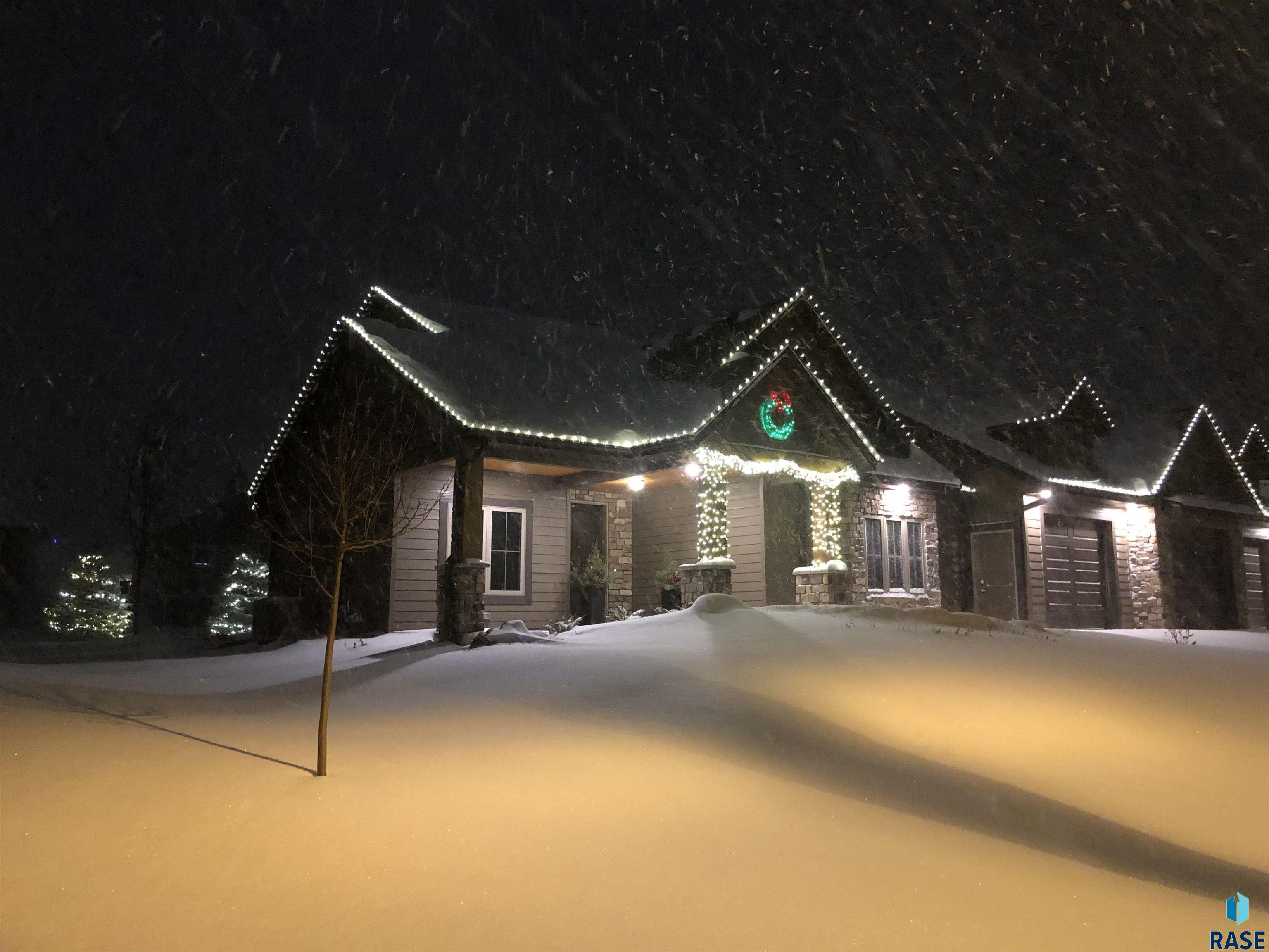 Snow-covered home at night with roofline holiday lights and a wreath above the entrance.