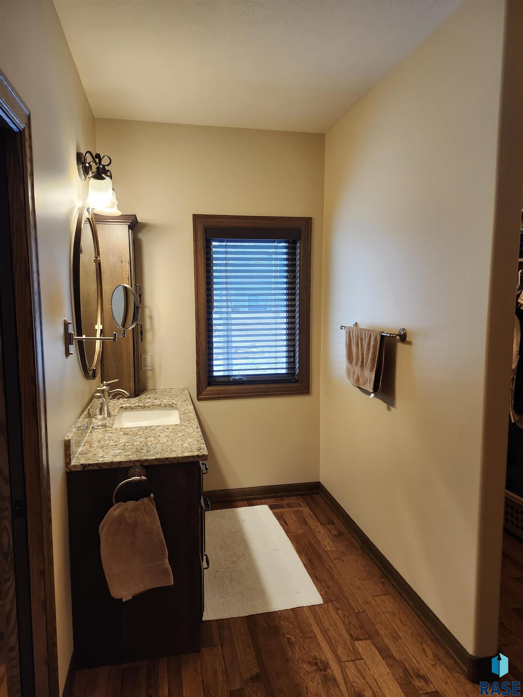 Bathroom with a granite vanity, dark wood cabinetry, and a window with blinds.