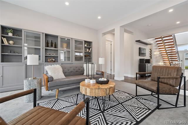 Living room with built-in shelving, gray sofa, geometric rug, and open-riser staircase.