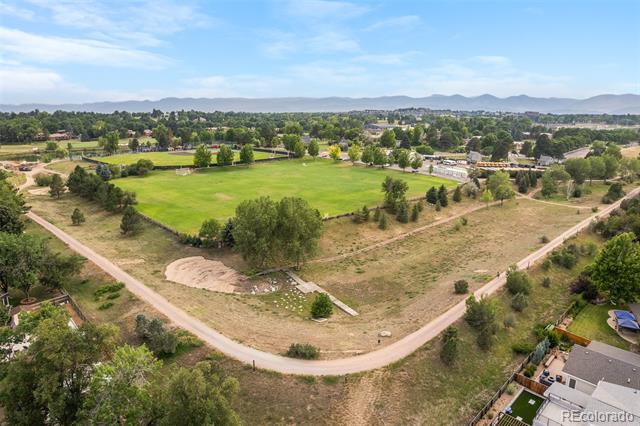 Aerial view of a green field and neighborhood, with tree-lined roads and distant mountains.