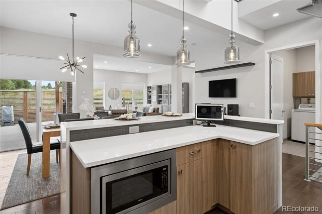 Open-plan kitchen with a large white island, wood cabinetry, and three pendant lights.
