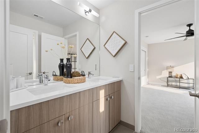 Bathroom with a double-sink wood vanity and mirror, opening to a carpeted bedroom.