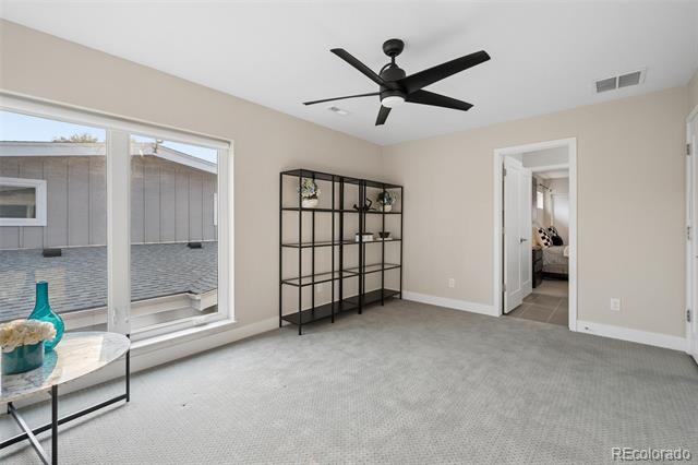 Carpeted room with a black ceiling fan and open shelving beside large windows.