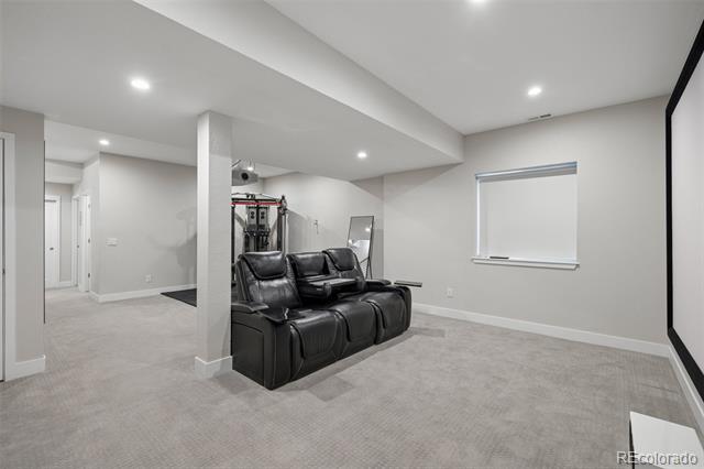 Finished basement living area with a black leather reclining sofa and exercise equipment.