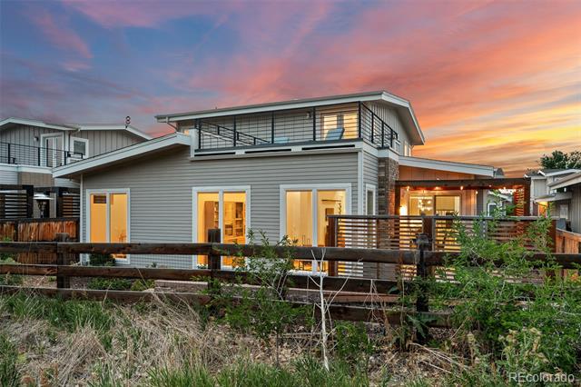 Modern gray home with large upper windows and a wood deck at dusk.