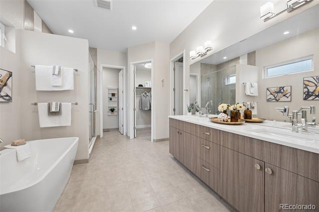 Bathroom with a bathtub and long double-sink vanity beneath a broad mirror.