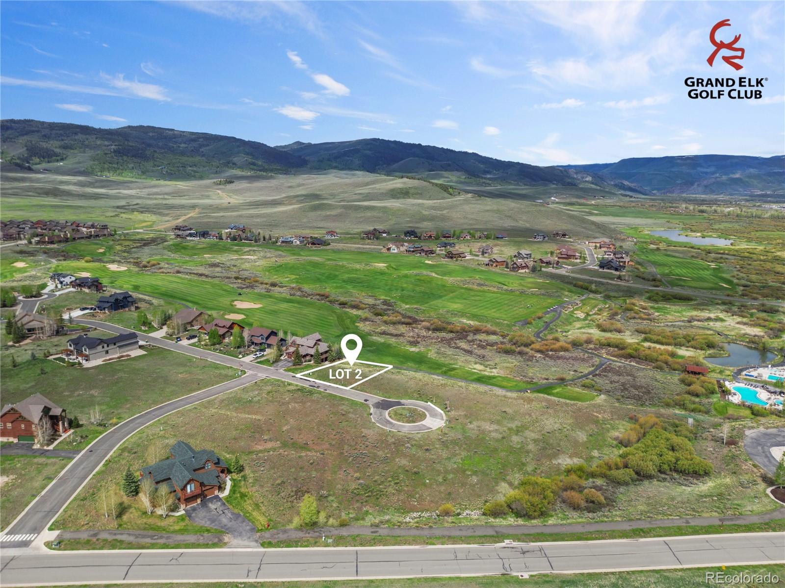 Aerial view of Lot 2 in a golf-course community, with surrounding homes and mountain ranges.