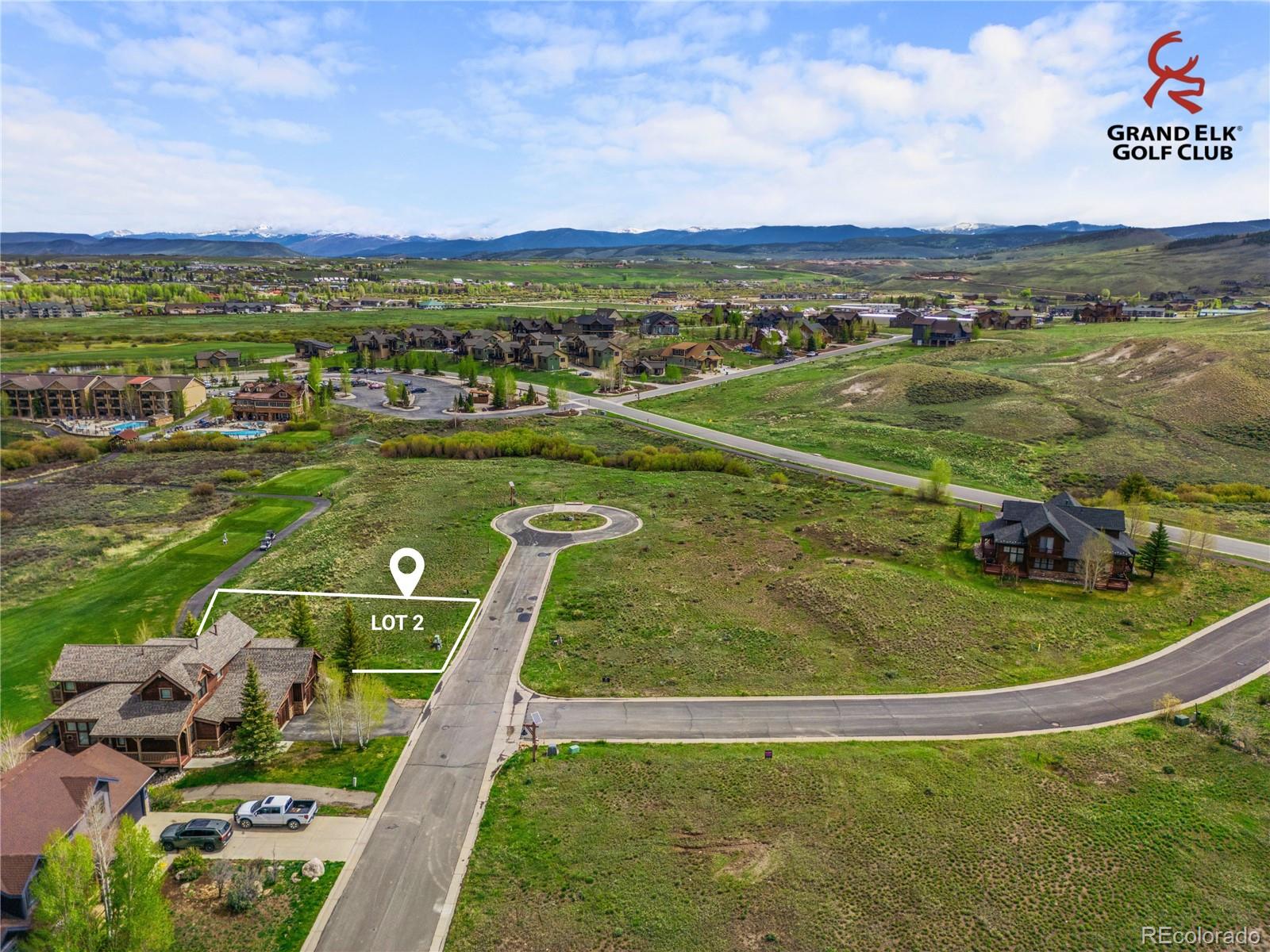 Aerial view of Lot 2 beside a residential street, with Grand Elk Golf Club and distant mountains beyond.