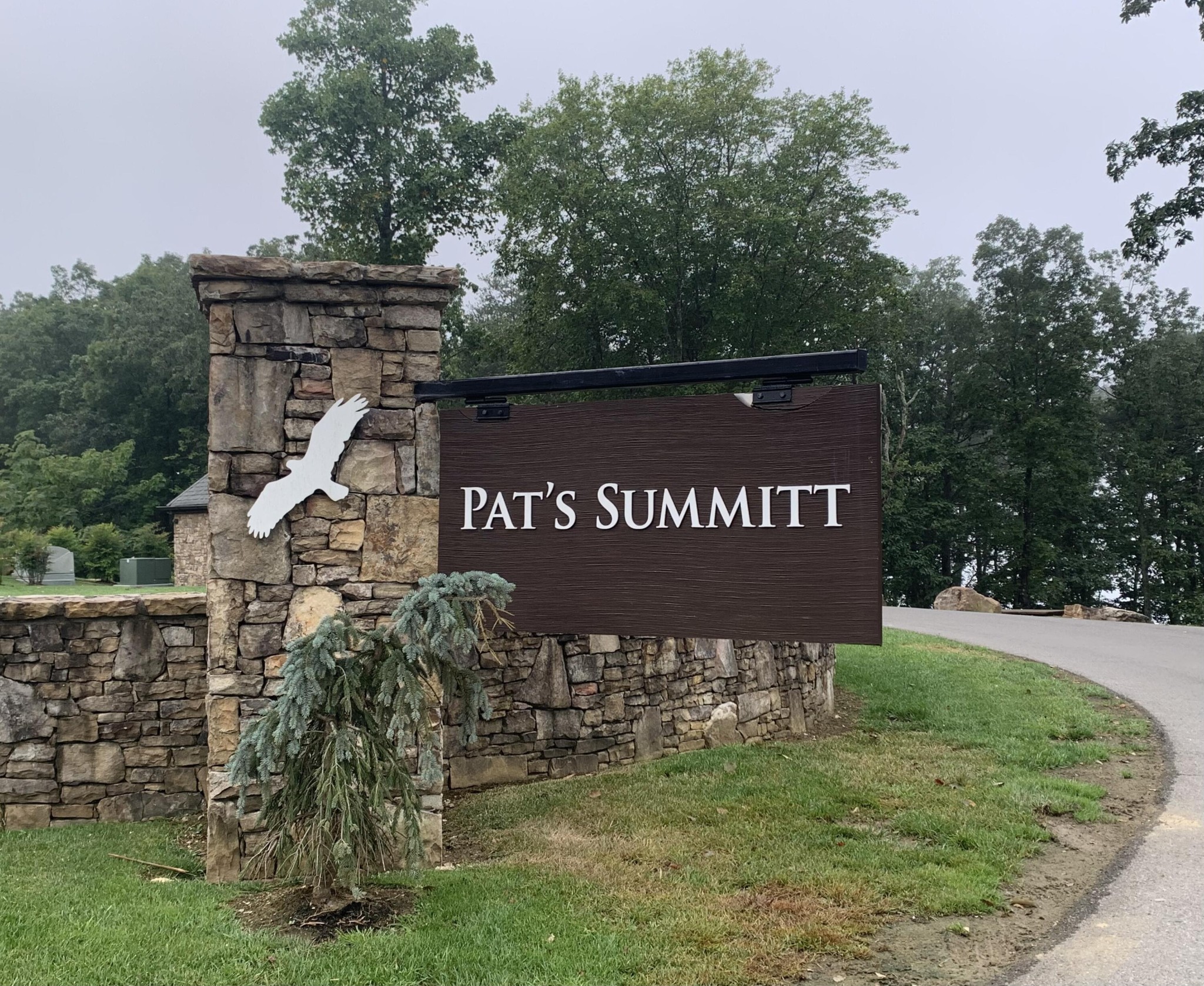 Pat’s Summit entrance sign on a stone wall beside a curving road.