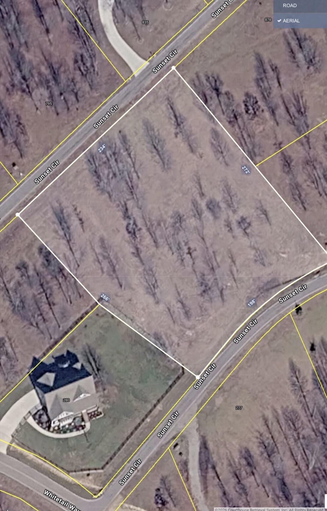 Aerial view of a wooded vacant lot outlined along Sunset Circle, beside a neighboring house.