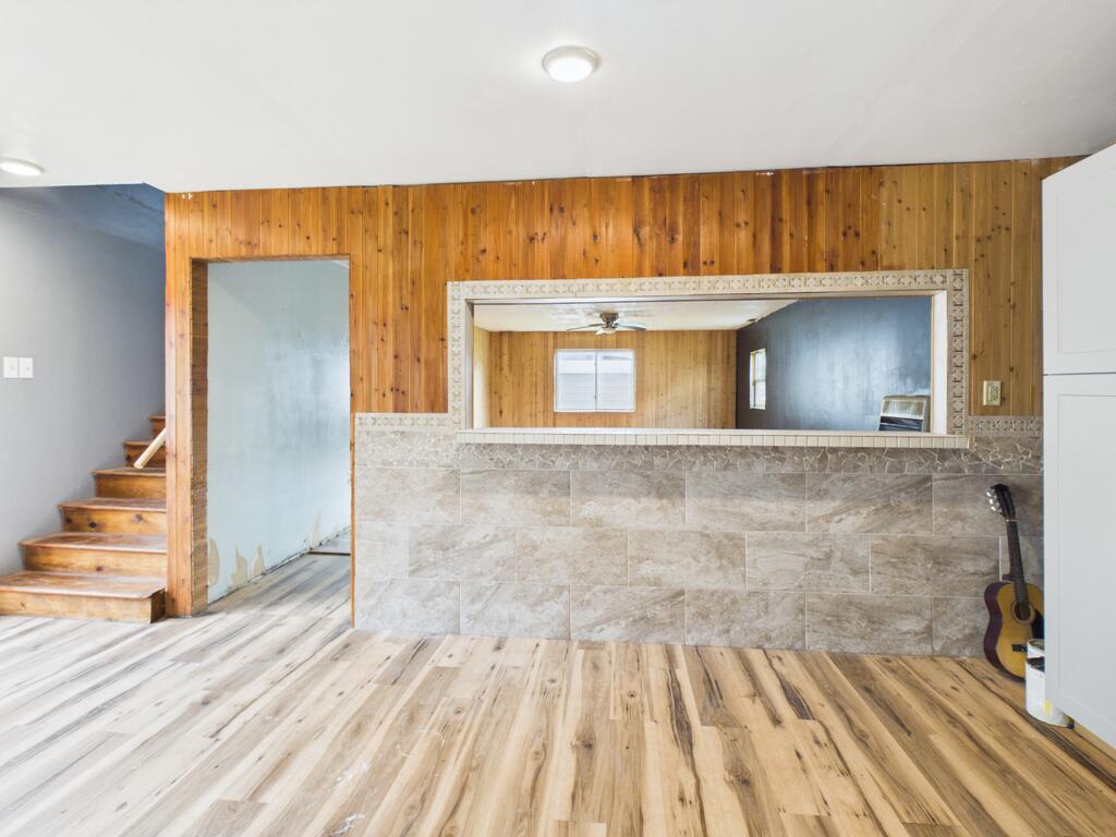 Open room with wood-paneled walls, tiled half wall, plank flooring, and staircase.