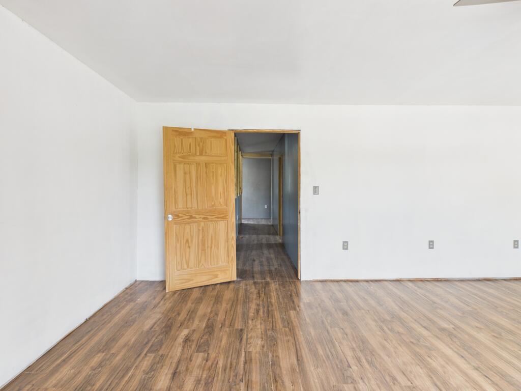 Vacant room with wood-look flooring and an open wooden door to the hallway.